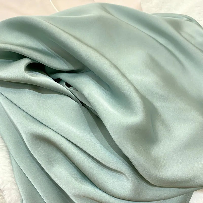 A close-up of draped satin fabric in a pale mint green color, showing its smooth texture and soft sheen.