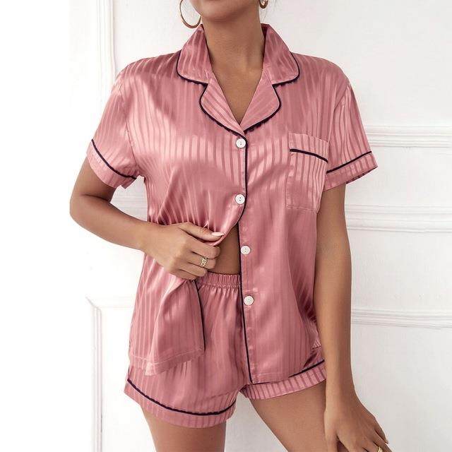 Pink satin pajama set with black piping worn by a model on a white background