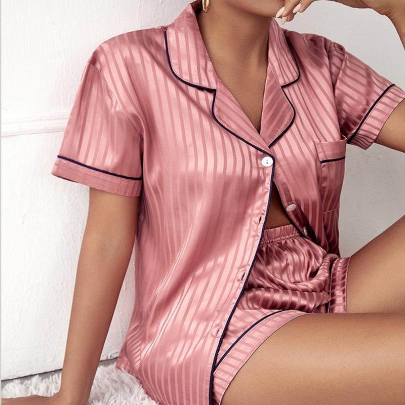 Pink satin pajama set with black piping worn by a person on a white background