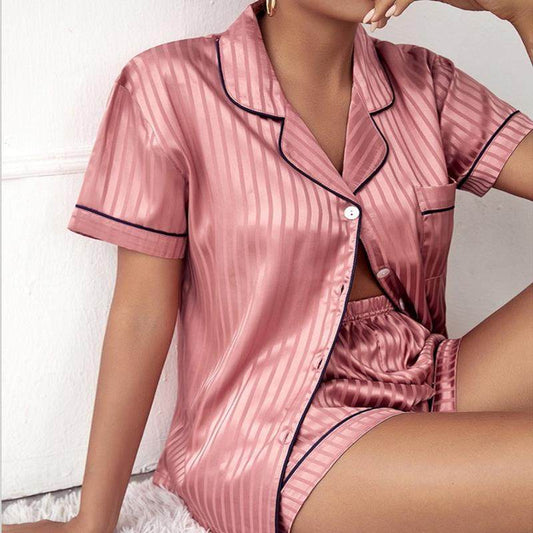 Pink satin pajama set with black piping worn by a person on a white background